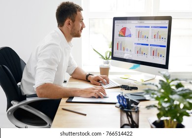Hombre de negocios joven que trabaja en la computadora en oficina. Retrato del hombre de negocios hermoso en la camisa blanca que se sienta en el escritorio del trabajo que mira el monitor. Imagen de alta calidad.