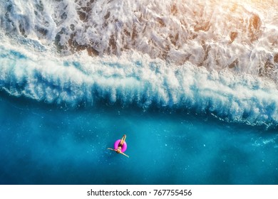 Luftaufnahme der jungen Frau, die auf dem rosa Schwimmring im transparenten türkisfarbenen Meer in Oludeniz schwimmt. Sommerseelandschaft mit Mädchen, Strand, schönen Wellen, blaues Wasser bei Sonnenuntergang. Draufsicht von der Drohne