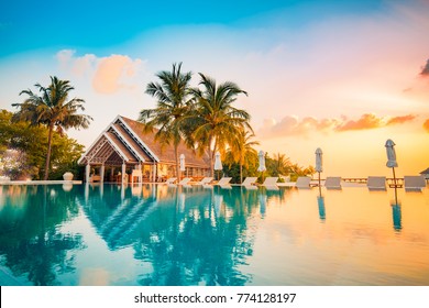 Beautiful poolside and sunset sky. Luxurious tropical beach landscape, deck chairs and loungers and water reflection.