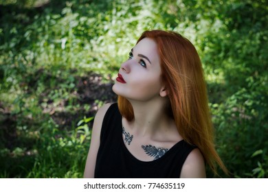 A young beautiful red hair girl with tattoes in a forest on a warm summer day. Not looking at the camera.