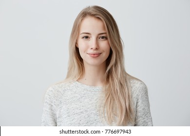 Pretty smiling joyfully female with fair hair, dressed casually, looking with satisfaction at camera, being happy. Studio shot of good-looking beautiful woman isolated against blank studio wall.