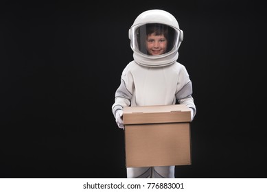 I am ready. Portrait of cheerful little spaceman wearing helmet and protective suit is standing and holding box while looking at camera with smile. Isolated with copy space. Resettlement concept