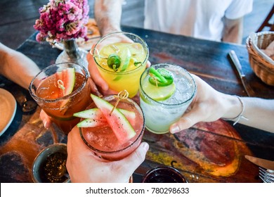 Friends toasting, saying cheers holding tropical blended fruit margaritas.  Watermelon and passionfruit drinks.