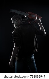 Horrible maniac with bloody chainsaw posing over dark background