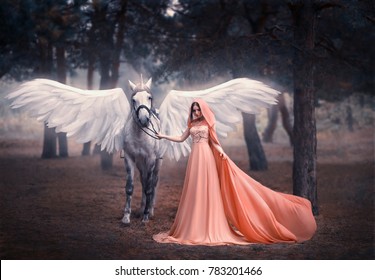 Beautiful, young elf, walking with a unicorn. She is dressed in a long orange dress with a cape, a hood. Artistic Photography