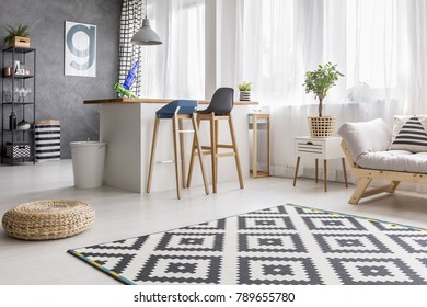 Open space living room interior with geometric carpet and dining area with barstools and white bin