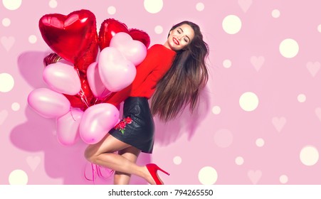 Valentine Beauty girl with red and pink air balloons laughing, on pink polka dots background. Beautiful Happy Young woman. holiday party. Joyful model posing, having fun, celebrating Valentine's Day