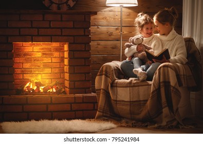 gelukkige familie moeder en kind dochter lezen een boek op winter herfstavond bij open haard