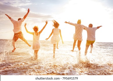 Eine Gruppe von fünf glücklichen Völkern rennt und springt zum Meeresstrand gegen Sonnenuntergangssonne
