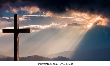 salib Yesus Kristus. Paskah, konsep kebangkitan. Salib kayu Kristen di latar belakang dengan pencahayaan dramatis, matahari terbenam gunung yang berwarna-warni, awan gelap dan langit, sinar matahari