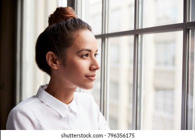 Jonge zakenvrouw met haar knot die uit het raam kijkt