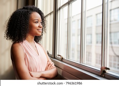 Jonge zwarte vrouw met gekruiste armen kijkt uit het raam