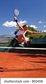Fată sărind peste fileu de tenis de bucurie în timp ce câștigă jocul în însorita Spaniei pe un teren de asfalt portocaliu.