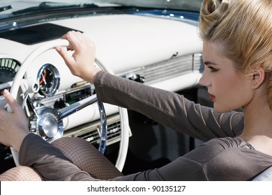 The beautiful girl, blond with visage and hair-up, sits in the old car. Wheel, dashboard, chrome.