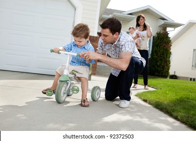 Father teaching his son to ride tricycle while wife standing in background