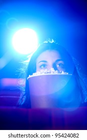 Une jolie jeune femme assise au cinéma, effrayée, se cache derrière une boîte de pop-corn.