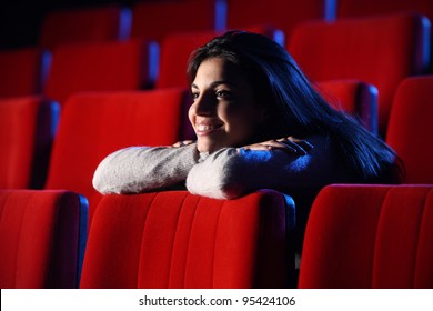 Lustiger Film: Porträt eines hübschen Mädchens in einem Kino, sie stützt ihre Ellbogen auf die hintere Stuhlreihe vor ihr, völlig entspannt.