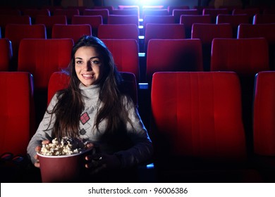 Ein hübsches Mädchen sitzt allein in einem leeren Kino, isst Popcorn und lächelt.
