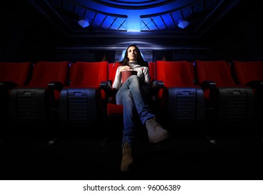 Eine hübsche junge Frau sitzt allein in einem leeren Kino und wartet auf den Film.