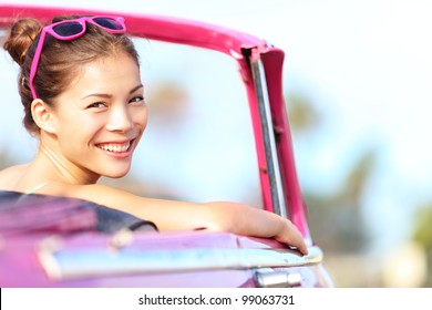 Autofrau glücklich in altem rosa Retro-Oldtimer. Junge Frau, die an einem schönen sonnigen Sommertag auf der Straße fährt. Ziemlich gemischtes asiatisches / kaukasisches weibliches Modell.