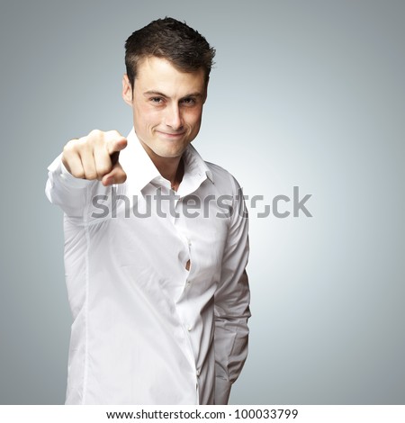 portraiit of a young man pointing with his finger against a grey background