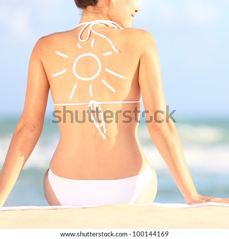 Sunscreen / sun tan lotion sun drawing on woman back. Girl in bikini sitting on beach in sunlight.
