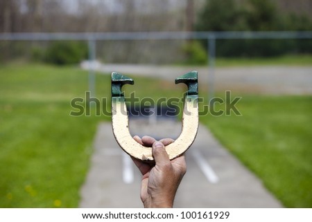 Player lines up to pitch a horseshoe in an outdoor court, hand and horseshoe in focus