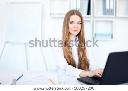 Portrait of beautiful young smiling business woman working on a laptop at bright office