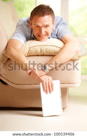 Man relaxing with tablet, laying on sofa in home with big window in background