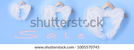 White angel wings from feather on hanger for clothes, light blue pastel colored background, Lettering "Sale"