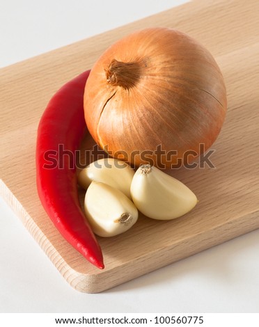 soft lights picture of a garlic cloves, onion and chili pepper on a wooden cutting board.