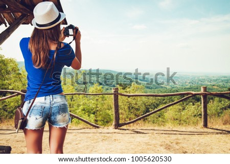Rear view of a young beautiful woman standing by viewpoint and taking photo for memory.
