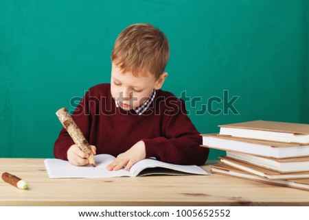 smiling little schoolboy writing notes in class against green background. A child draws in a notebook with a pencil. School concept. Back to School. school change Royalty-Free Stock Photo #1005652552