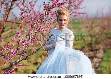 beautiful blonde bride in a chiffon blue dress to walk along the flowering pink spring garden. portrait of a girl with a hairdo and decorations in her hair.