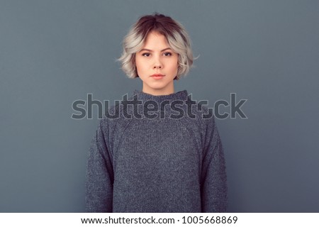 Young woman in a grey sweater studio picture isolated on grey background serious