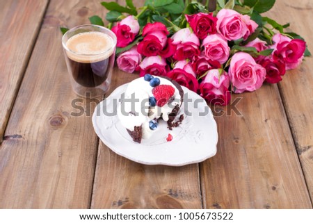 Sweet cake with cream and berries on a white plate. A bouquet of rosé roses and a glass with espresso coffee. Wooden background. Free space for text or postcards.