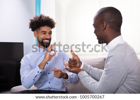 Two Young Happy Men Sitting On The Sofa Making Sign Languages