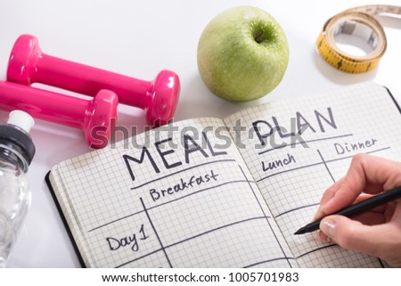 High Angle View Of A Person Hand Filling Meal Plan In Notebook At Wooden Desk Royalty-Free Stock Photo #1005701983
