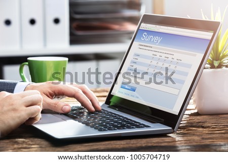Close-up Of A Businessperson's Hand Filling Online Survey Form On Laptop Over Wooden Desk Royalty-Free Stock Photo #1005704719