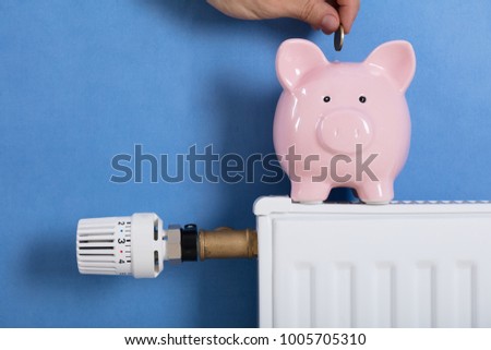 Close-up Of Person Man Inserting Coin In Piggy Bank Kept On Radiator