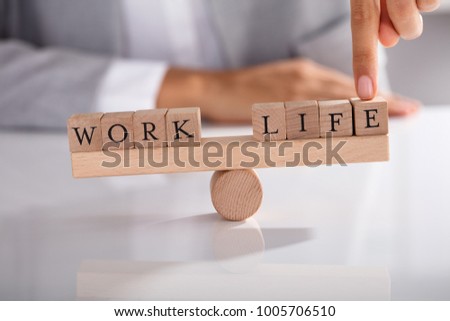 Close-up Of Businessperson's Finger Showing Imbalance Between Work And Life On Wooden Seesaw