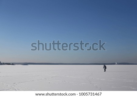 Man is ice-skating on a desolate lake against a blue sky on a sunny day