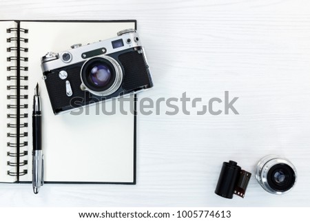 vintage camera, lens, negative film, open notepad with fountain pen on white wooden desk, flat lay