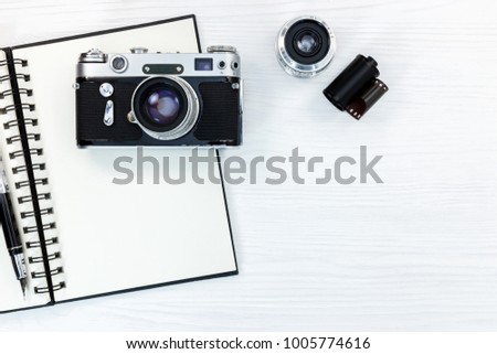 old photo camera, lens, film roll, notebook and pen on white wooden background flat view
