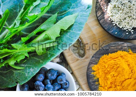 Health collage of leafy greens and super foods including collard greens, dandelion greens hemp seeds, antioxidant blueberries and anti-inflammatory turmeric on stones and a rustic wood cutting board. Royalty-Free Stock Photo #1005784210
