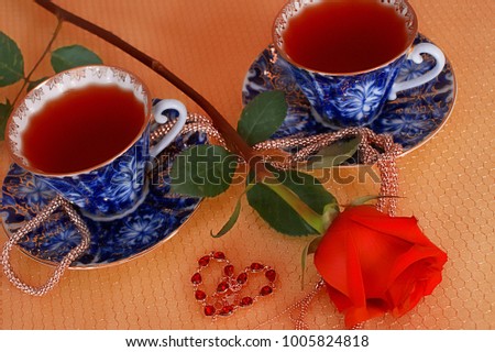 Two cups of tea and a beautiful red rose next to them with the little heart on a golden grid