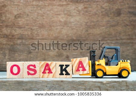 Yellow toy forklift hold letter block A to complete word Osaka on wood background