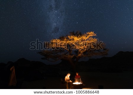 Couple at campfire, camping under starry sky and Milky Way arch. Adventure into the wild, Namibia road trip, vacation in Africa.