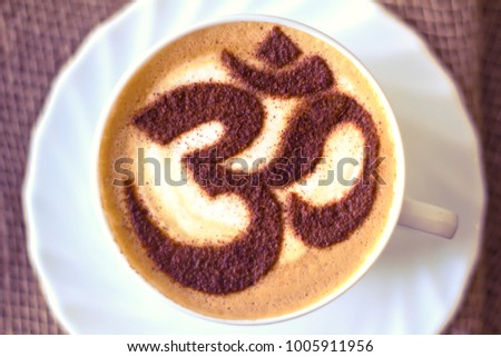 a sign of OUM on a foam of hot cappuccino in a white cup and stars on a dark table