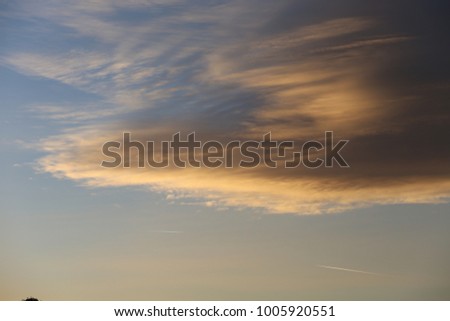 Close up view of big grey and black clouds in a blue sky. Lengthered forms lighted by the rising sun in the morning. Peaceful and calm image. Abstract textured natural surface. Bright colors.  
